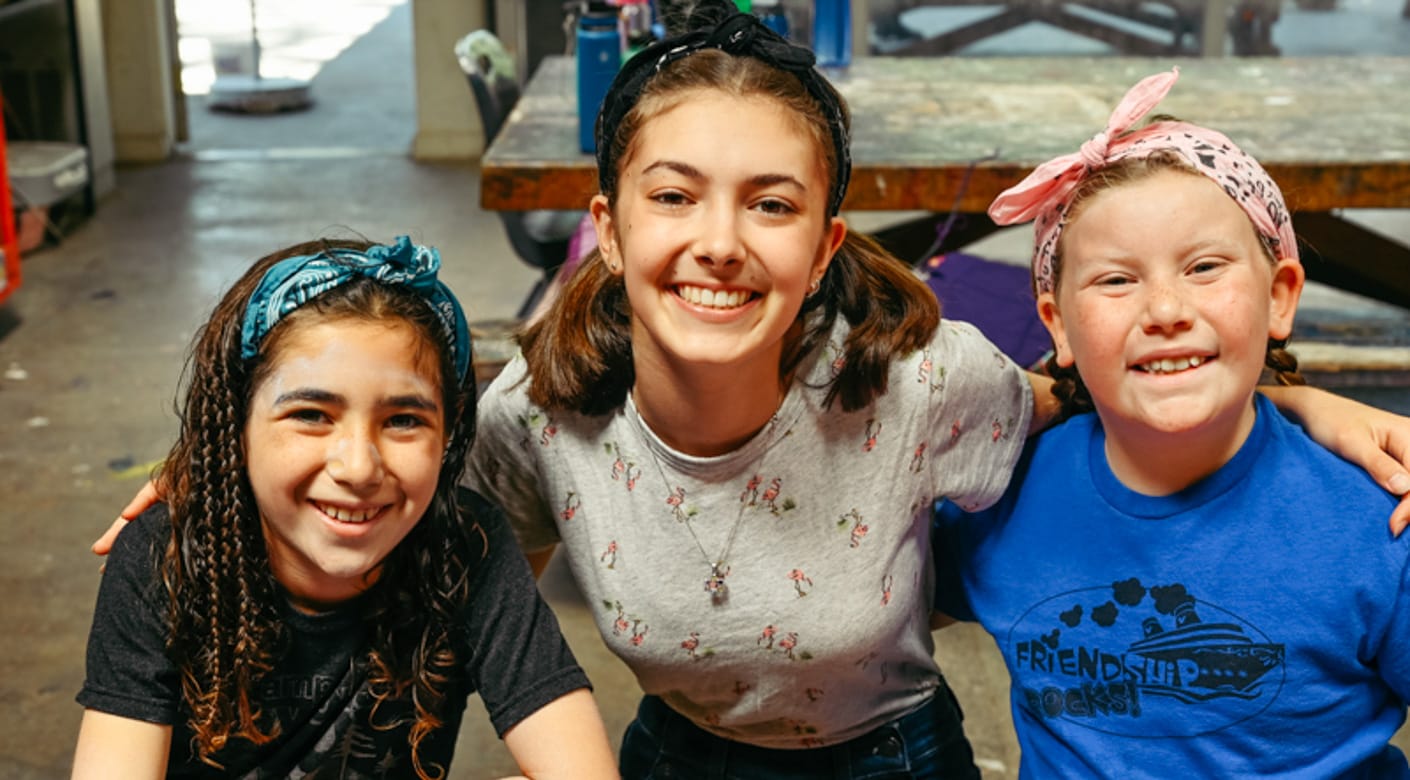 Counselor in training with female campers at arts and crafts smiling