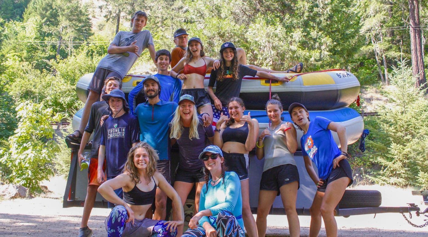 Group of teens on an adventure quest standing beside a van with a raft on top