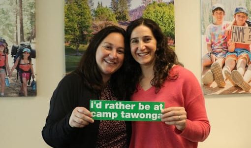 Two year-round Tawonga staff members holding a sign that says "I'd rather be at Tawonga"