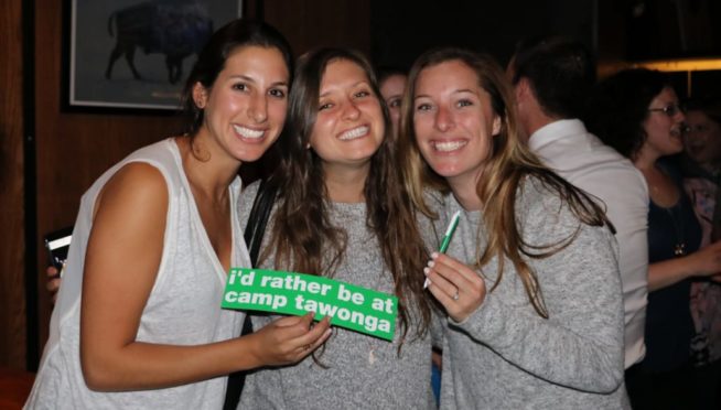 Three female alumni holding a Tawonga sign